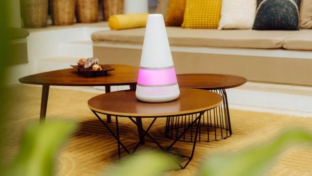 Ein weißer Luftbefeuchter mit rosa Licht steht auf einem runden Tisch.