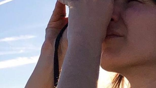 Eine Frau blickt durch ein großes, schwarzes Objektiv in den Himmel.