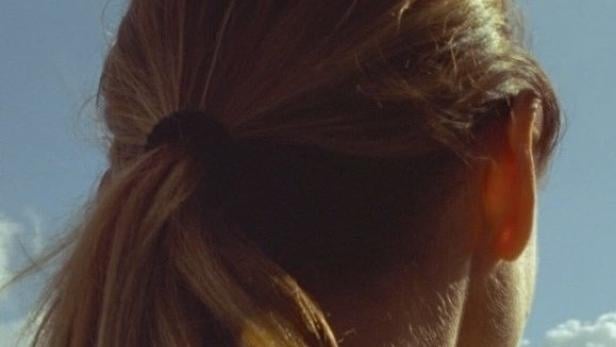 Eine Frau mit blonden Haaren blickt in den blauen Himmel.