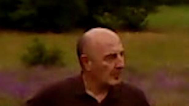 Ein Mann mit Glatze lehnt an einem Zaun und schaut nach rechts.