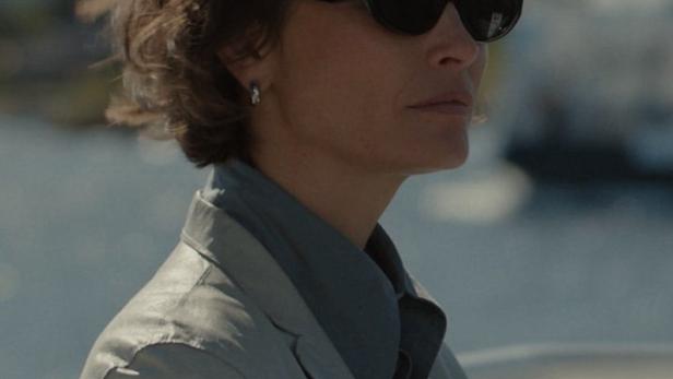 Eine Frau mit Sonnenbrille und Blazer an Bord eines Schiffes.