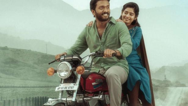 Ein Mann und eine Frau fahren auf einem Motorrad durch eine hügelige Landschaft.