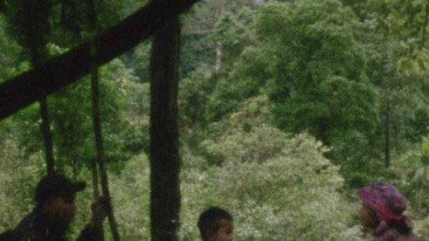 Eine Familie sitzt auf einem Floß auf einem ruhigen Gewässer, umgeben von üppigem Grün.