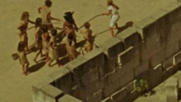 Eine Gruppe von Kindern spielt mit einer Frau in einer alten Festung.