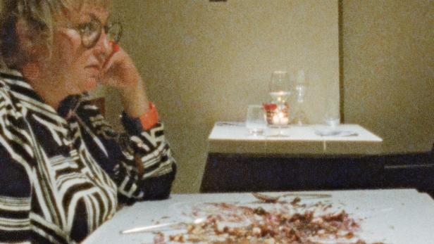 Eine Frau sitzt an einem Tisch mit Essensresten und wirkt nachdenklich.