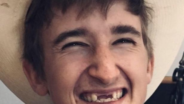 Ein lächelnder junger Mann mit Hut und gestreiftem Hemd.