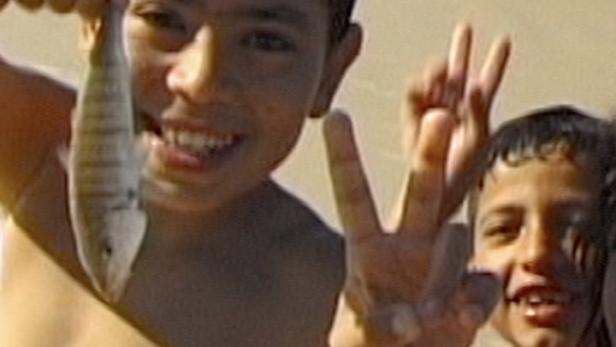 Ein Junge hält einen Fisch am Strand, während ein anderer Junge ein Victory-Zeichen macht.