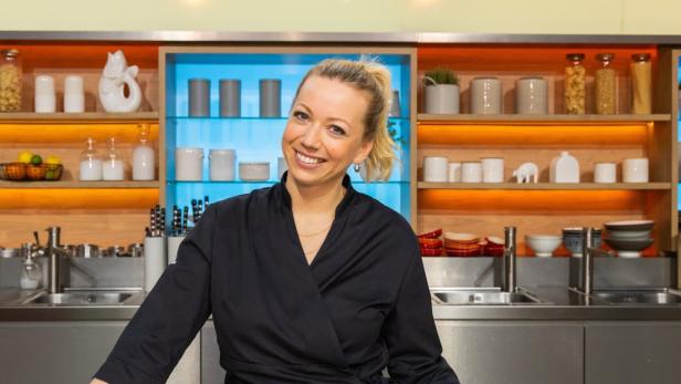 Eine lächelnde Frau in Kochkleidung steht in einer Küche.