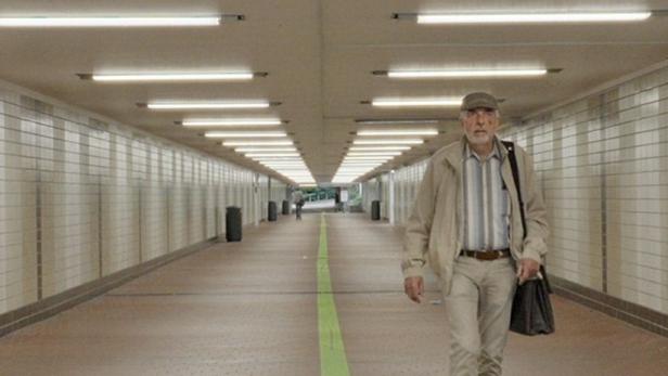 Ein Mann geht in einer Unterführung an einer grünen Linie entlang.