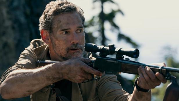 Ein Mann zielt mit einem Gewehr mit Zielfernrohr in einer bewaldeten Umgebung.