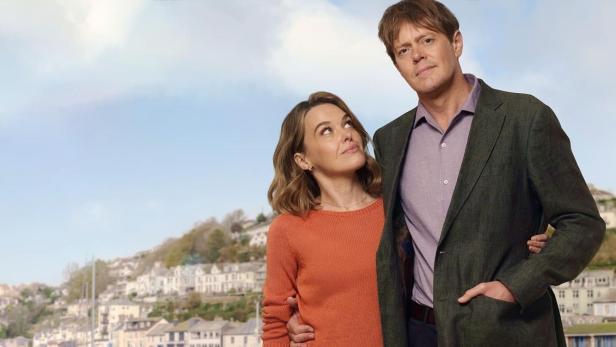 Ein Paar steht vor der Kulisse von Shipton Abbott, Devon, mit dem Titel „Beyond Paradise“ im Himmel.