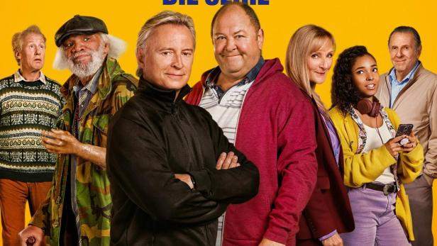 Das Filmplakat zur Serie „Ganz oder gar nicht“ zeigt eine Gruppe von Personen und einen Hund vor gelbem Hintergrund.