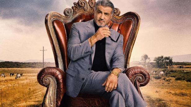 Sylvester Stallone sitzt als „Tulsa King“ auf einem Thron inmitten einer ländlichen Szene.