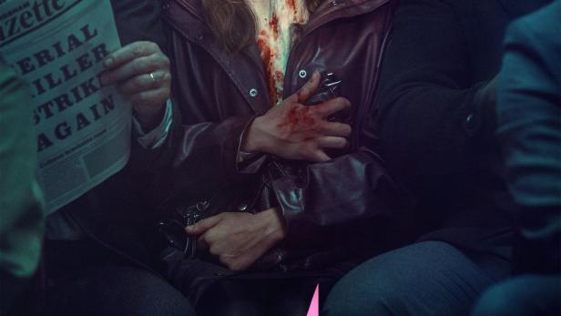 Eine Frau mit blutverschmierter Bluse sitzt zwischen zwei Männern in einem Zug.