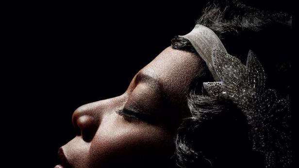 Porträt einer Frau mit Stirnband und Ohrring vor schwarzem Hintergrund. Über ihr steht der Name „Bessie“.