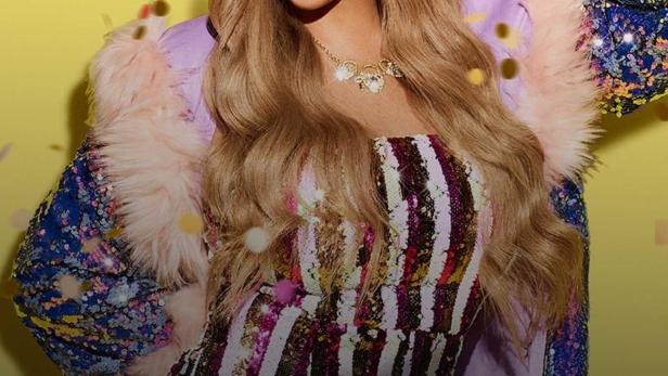 Charlotte Crosby mit Krone und Paillettenjacke vor gelbem Hintergrund mit Konfetti.