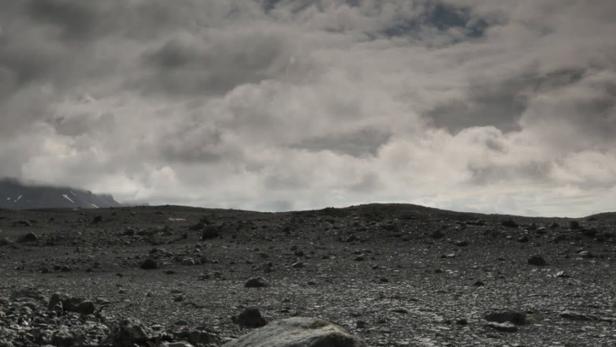 Eine karge Landschaft mit Steinen unter einem bewölkten Himmel und strahlender Sonne.