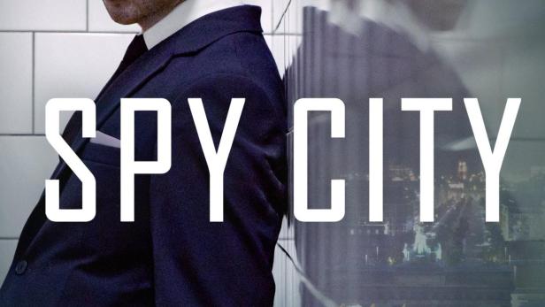 Das Filmplakat für „Spy City“ zeigt einen Mann im Anzug vor einer Berliner Stadtansicht.