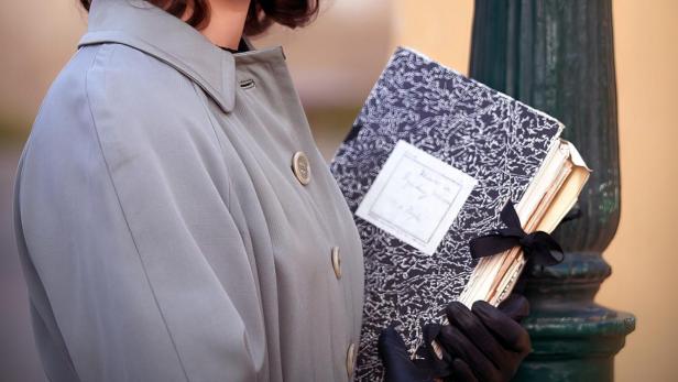 Eine junge Frau im Stil der 1950er Jahre mit Notizbüchern vor einer Strassenlaterne.