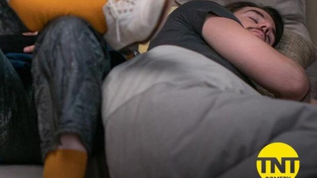 Eine Frau mit gelben Socken legt ihre Füße auf einen schlafenden Mann.