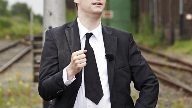 Ein Mann im Anzug steht vor einem alten Bahnhofsgelände.