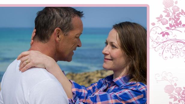 Ein Paar umarmt sich am Strand, im Hintergrund das Meer.