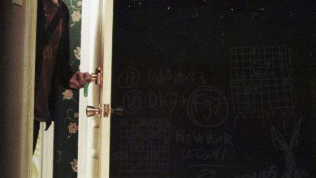 Ein Mann steht in einer Tür; im Hintergrund eine Wand mit der Aufschrift „5150, Rue des Ormes“.