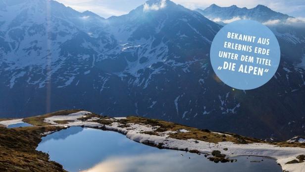 Das Cover der Dokumentation „Wilde Alpen“ zeigt eine Berglandschaft mit einem kleinen See.