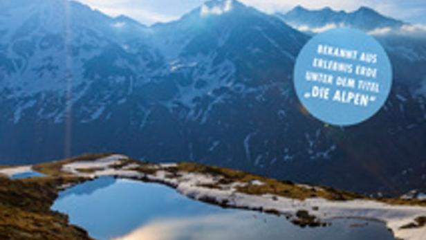 Das Cover der Dokumentation „Wilde Alpen“ zeigt eine Berglandschaft mit einem kleinen See.