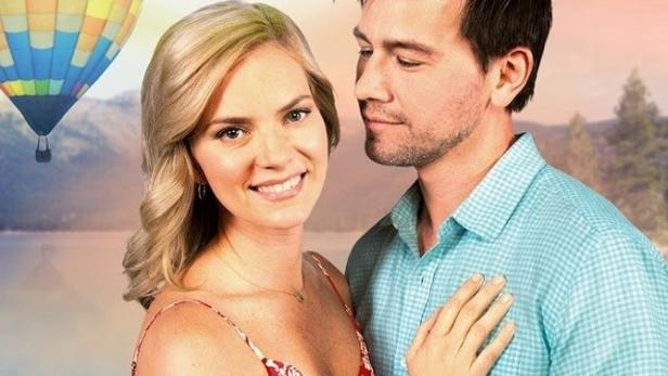 Ein Paar umarmt sich vor einem See und einem Heißluftballon, im Hintergrund der Titel „Romance in the Air“.