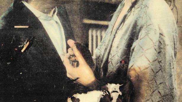 Ein Mann mit Hut und eine Frau stehen sich auf dem Filmplakat „Brennende Betten“ gegenüber.