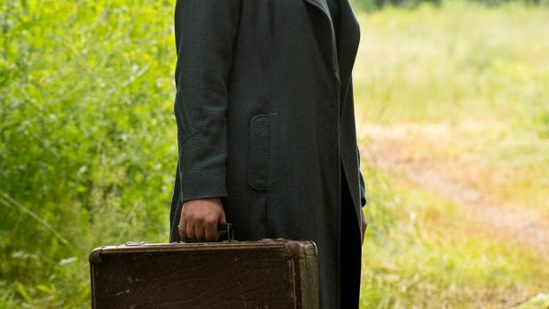 Eine Frau mit einem alten Koffer steht auf einer Wiese.