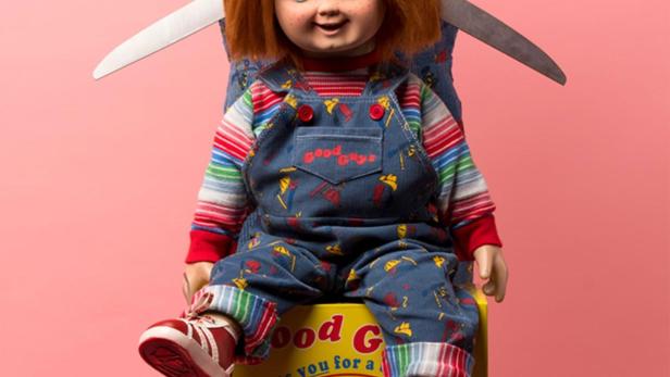 Eine Frau hält eine übergroße Schere hinter dem „Chucky“-Puppe, die auf einer Kiste sitzt, mit dem Titel „Living with Chucky“.