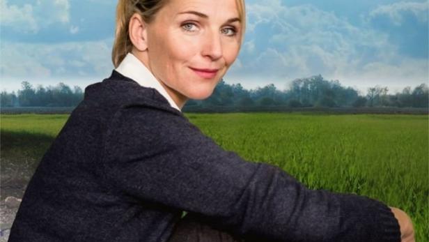 Eine Frau sitzt vor einer grünen Wiese und einem bewölkten Himmel.