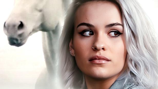 Eine junge Frau mit silbernem Haar und ein weißes Pferd im Hintergrund, möglicherweise ein Filmposter für „Mystic“.
