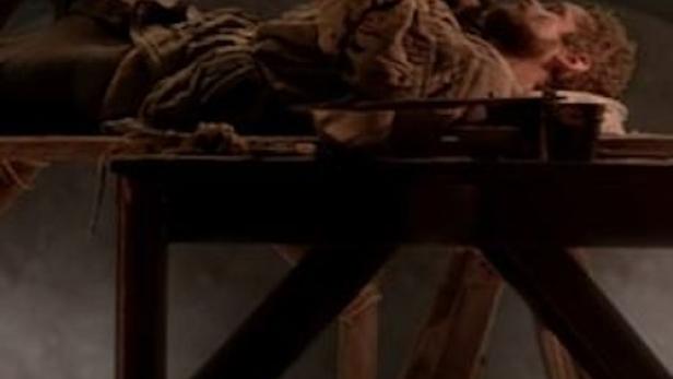 Ein Mann liegt auf einem Gerüst und malt ein Deckengemälde.