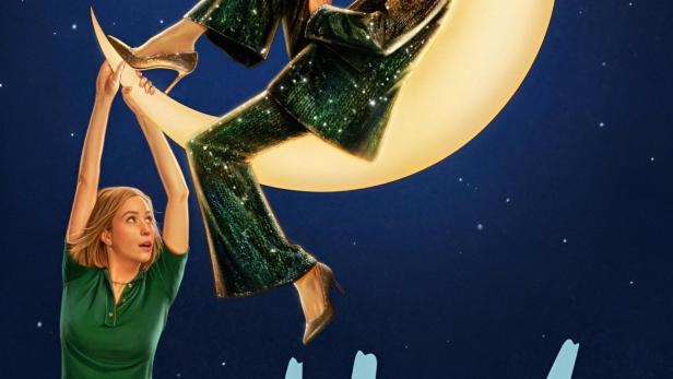 Eine Frau hält einen Halbmond, auf dem eine andere Frau in einem glitzernden Hosenanzug sitzt.