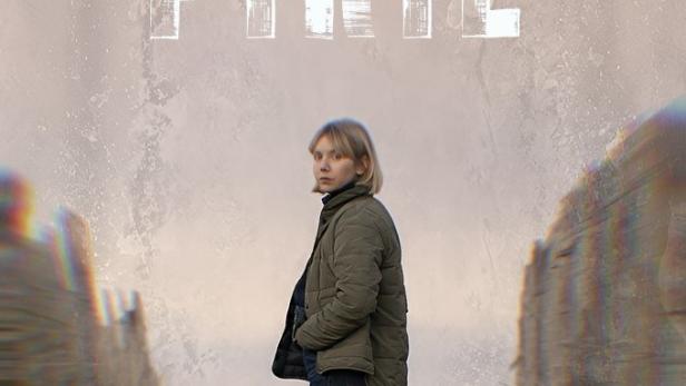 Eine Frau steht vor dem Hintergrund des Titels „Karen Pirie“ auf einem sandigen Weg.