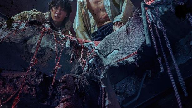 Drei Personen befinden sich inmitten von Trümmern, möglicherweise nach einer Katastrophe.