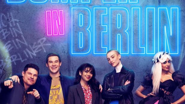 Die Besetzung von „Pitch Perfect: Bumper in Berlin“ vor einem neonbeleuchteten Titel.
