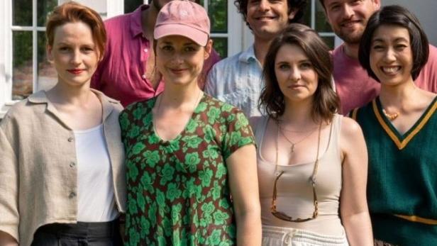 Eine Gruppe von sieben Personen steht vor einem Haus mit bunten Girlanden.