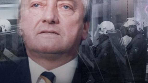 Ein Porträt eines Mannes vor dem Hintergrund einer Demonstration mit Polizisten.