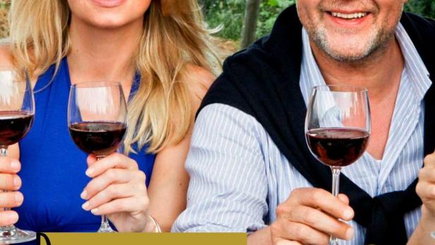 Ein Mann und eine Frau sitzen mit Weingläsern und Speisen vor einem Weinberg.