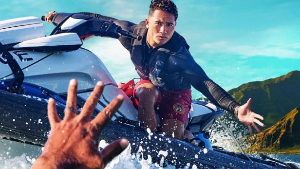 Ein Rettungsschwimmer auf einem Jetski streckt seine Hand nach einer Person im Wasser aus.