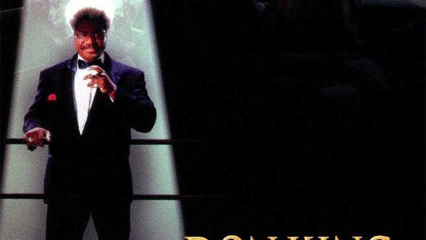 Don King steht im Boxring, im Hintergrund ein Boxer im Schatten.