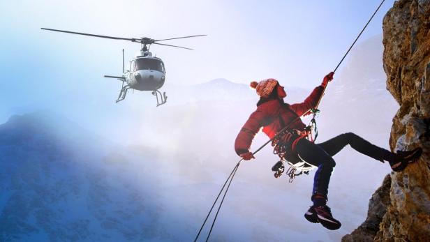 Eine Person seilt sich von einer Klippe ab, während ein Hubschrauber in der Nähe schwebt.
