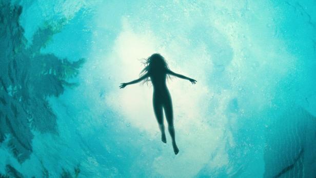 Eine Frau schwimmt unter Wasser; im Hintergrund der Titel „Saint X“.