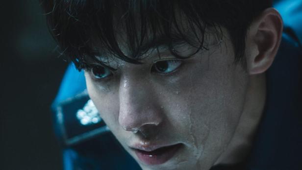 Ein verschwitzter, junger Polizist blickt ernst nach unten.