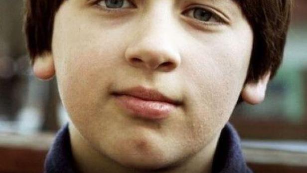 Ein junger Mann mit braunen Haaren und blauen Augen blickt in die Kamera.