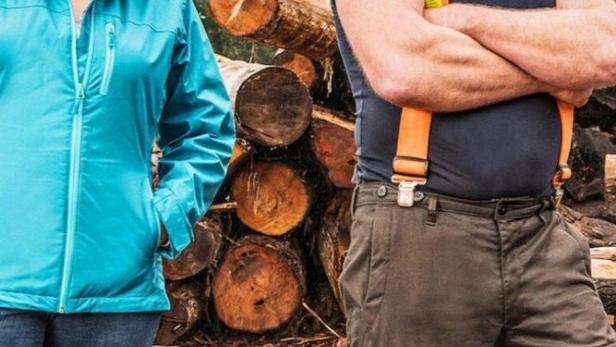 Ein Mann mit Schutzhelm und eine Frau stehen vor einem Stapel Baumstämme für die Sendung „Big Timber“.